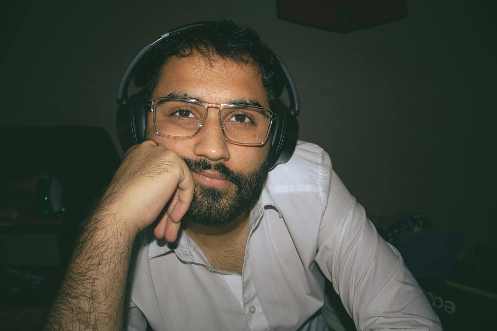 A thoughtful bearded man with glasses and headphones in a casual portrait setting.